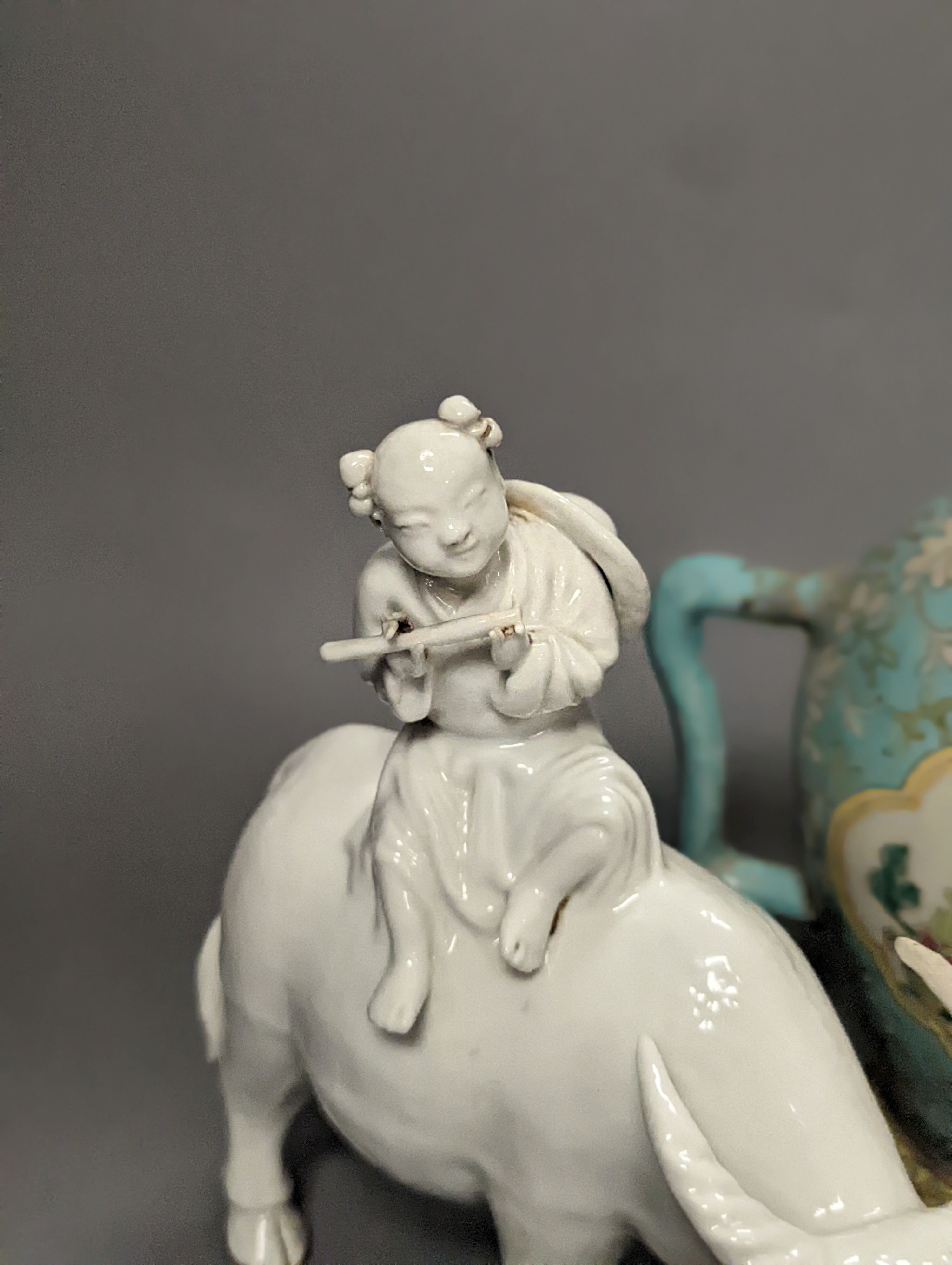 A 19th century Cadogan shape Chinese wine ewer, a Chinese blanc de chine figure riding an ox, an 18th century Chinese miniature blue ground ‘cockerel’ teapot and a Japanese Daikoku figural box and cover. Tallest 19cm